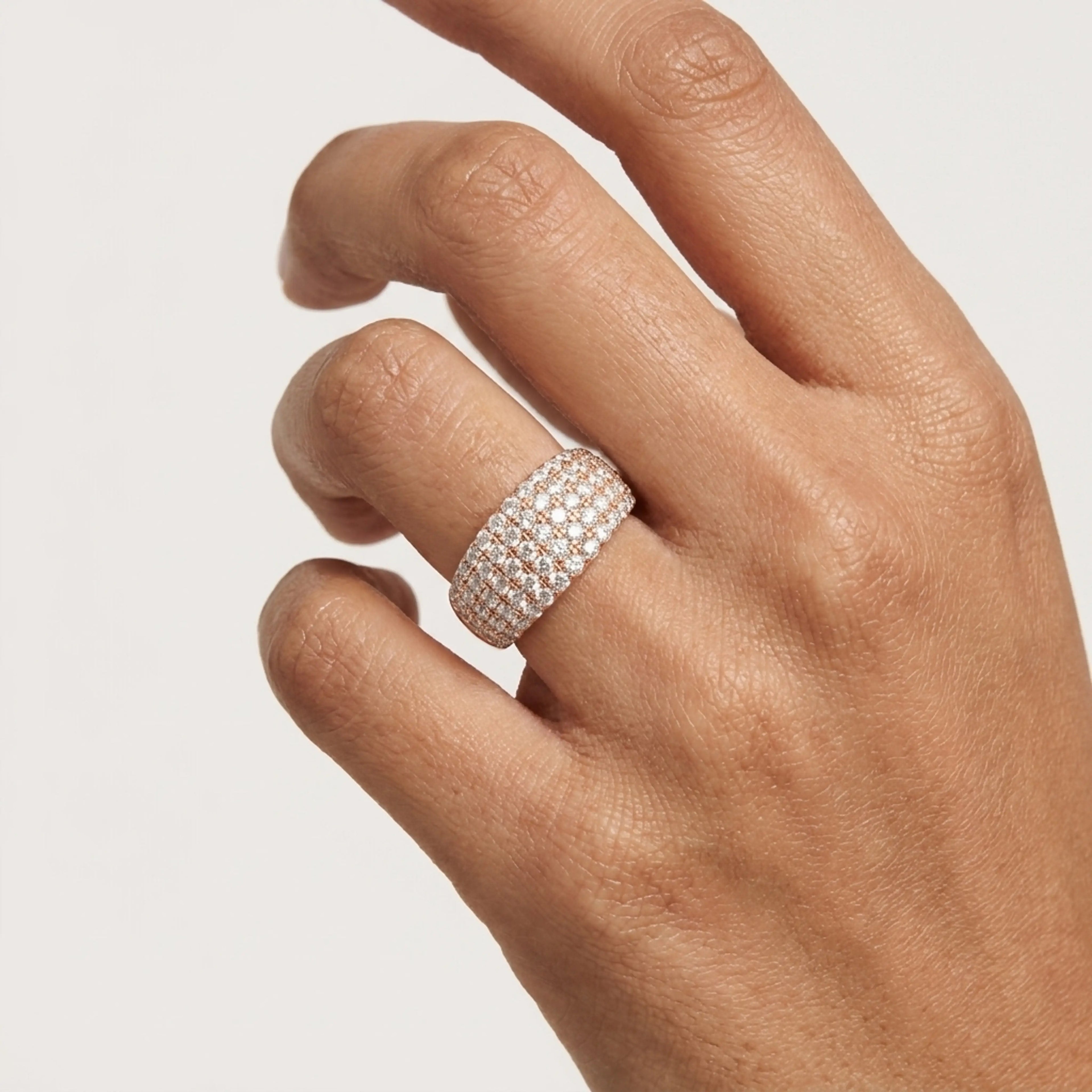 A close-up of a hand wearing a wide gold band ring set with multiple rows of small clear diamonds, photographed against a plain light background.