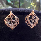 Pair of rose gold earrings with intricate designs on a black background