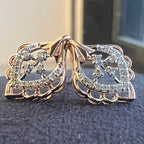 Pair of rose gold earrings with diamond accents on a dark surface.