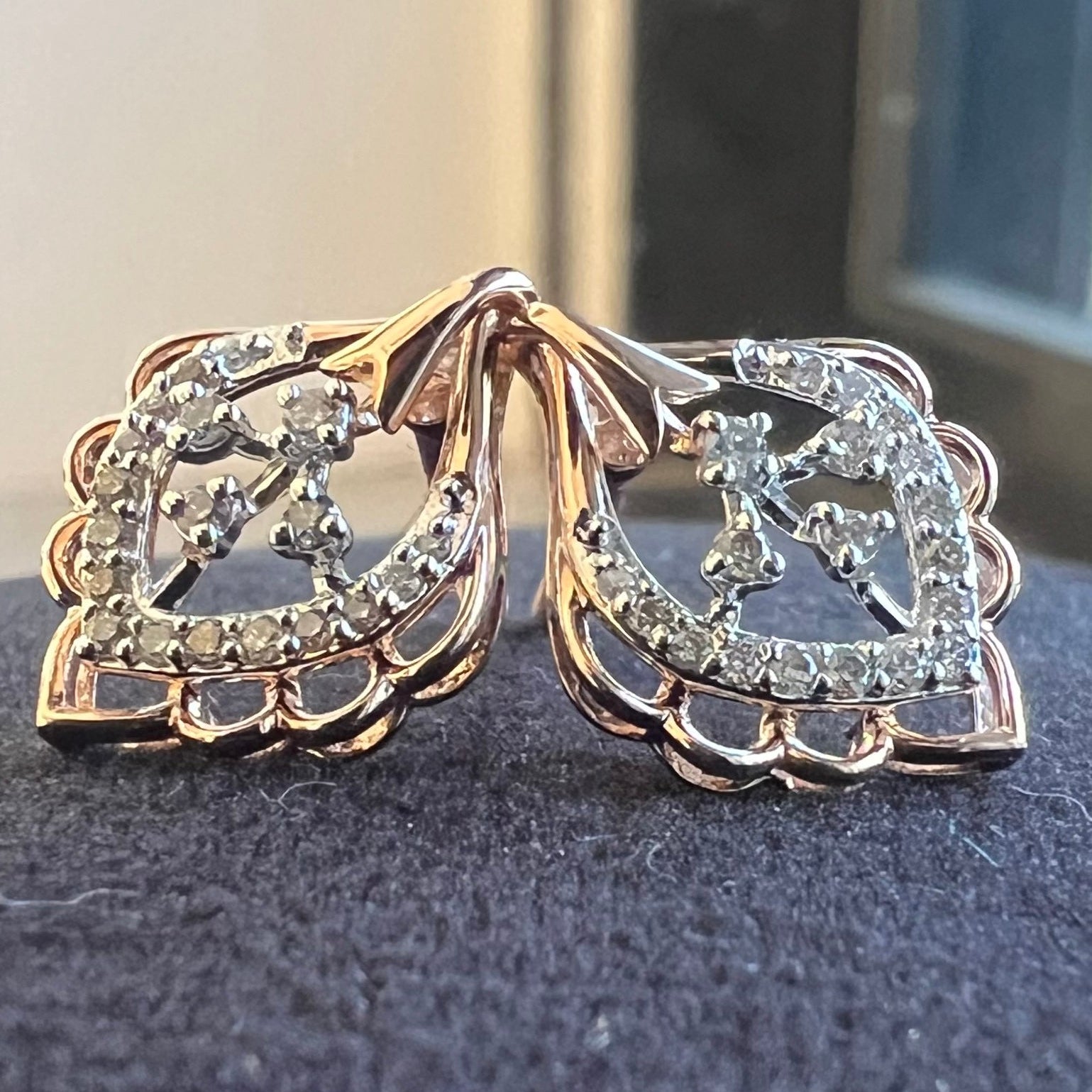 Pair of rose gold earrings with diamond accents on a dark surface.