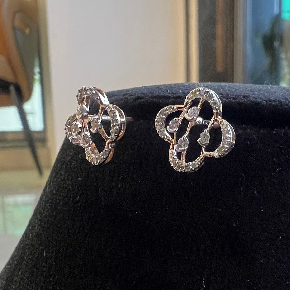 Pair of gold earrings with diamond accents on a black stand.