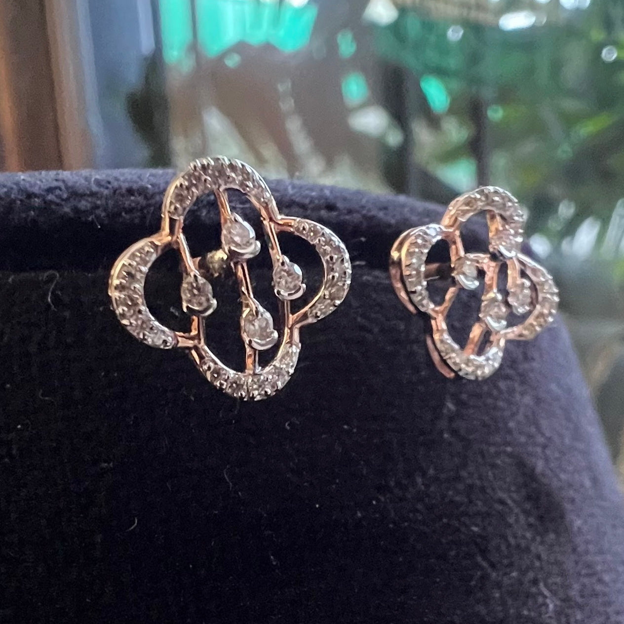 Pair of gold earrings with diamonds on a black stand.