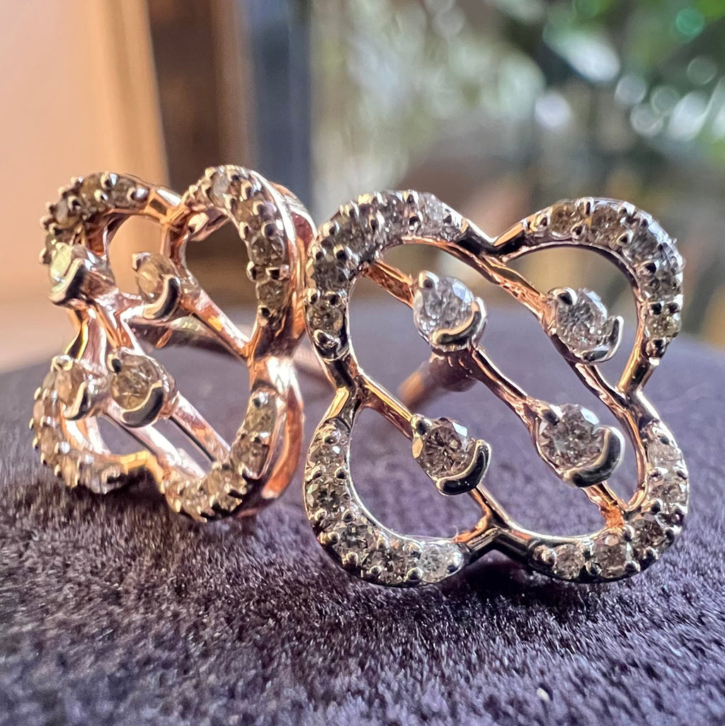Rose gold butterfly-shaped earrings with embedded diamonds on a dark surface.