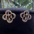 Pair of diamond earrings on a black cushion with a blurred green background