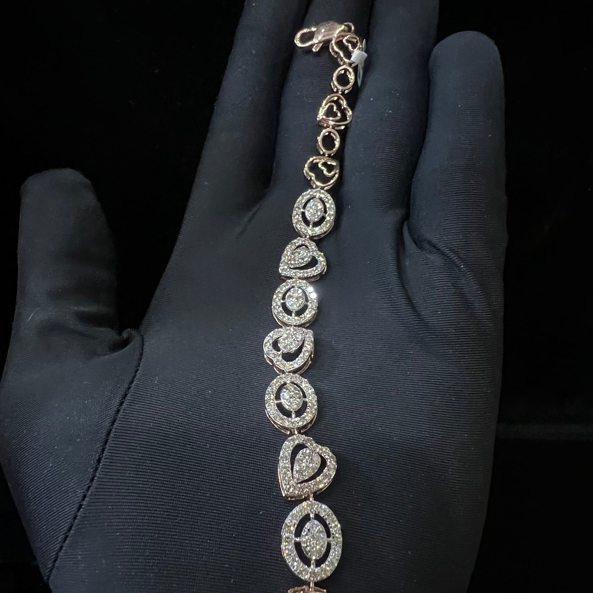 Gold bracelet with heart designs on a hand wearing a black glove against a dark background