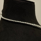 White gold beaded diamond tennis necklace on a black mannequin against a neutral background