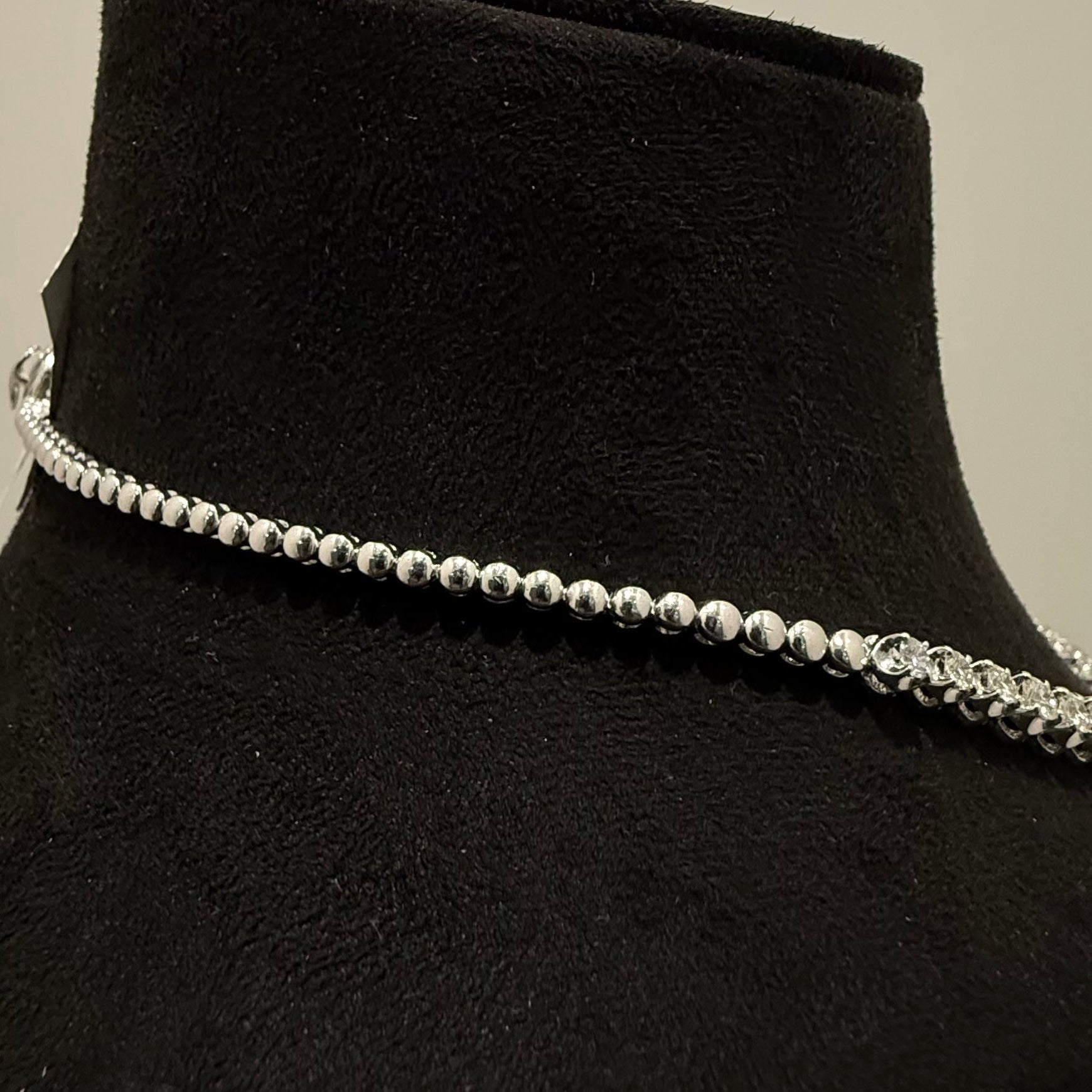 White gold beaded diamond tennis necklace on a black mannequin against a neutral background