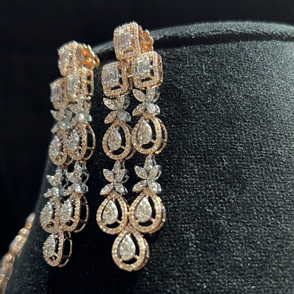 Pair of gold and diamond earrings on a black stand.
